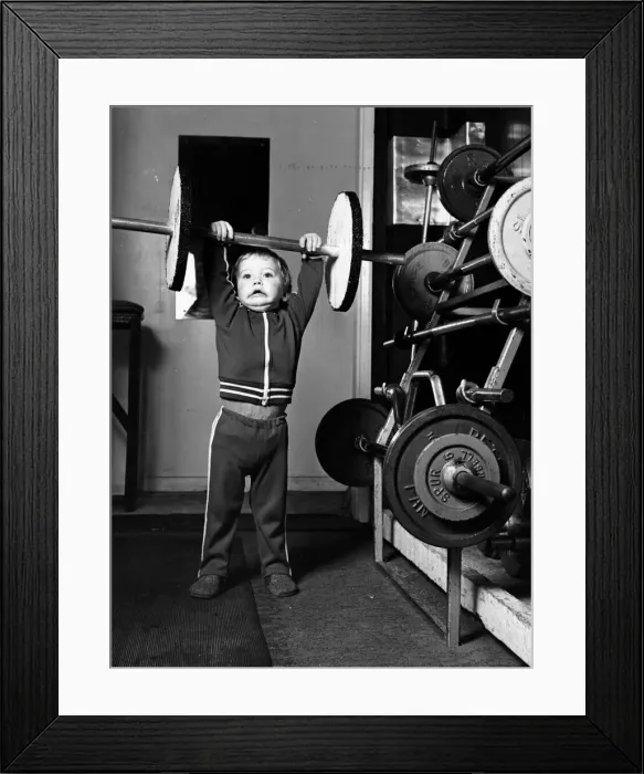 Framed Print : Two and half year old boy Ian Page lifts a set odf special wooden weights built for him Framed Print : Two and half year old boy Ian Page lifts a set odf special wooden weights built for him