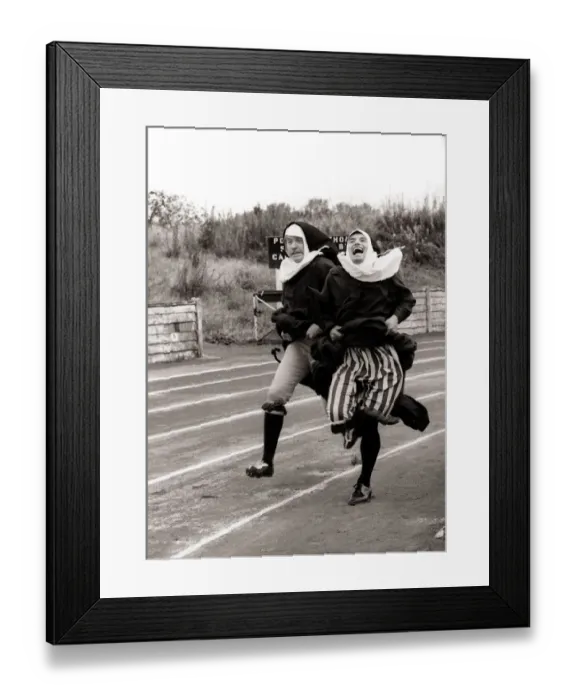Framed Print : Kevin Moran and David Cannon dressed as Nuns hold on to their skirts in the 100m dash