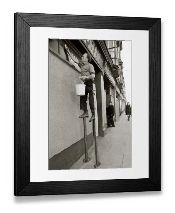 Framed Print : George Pettican Window Cleaner on Stilts cleaning windows on the front of his shop in Framed Print : George Pettican Window Cleaner on Stilts cleaning windows on the front of his shop in