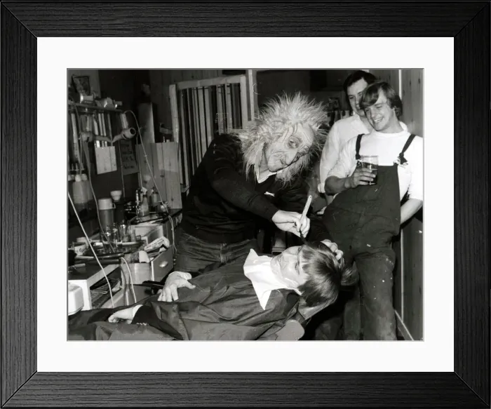 Framed Print : A customer sits in the barbers chair having his faced shaved by a man in a mask at Steve
