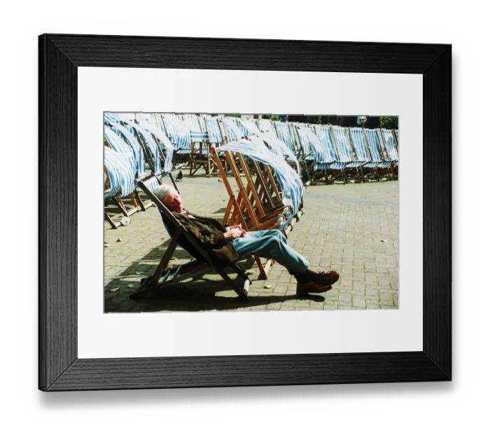 Framed Print : Man sleeping on deckchair in a London park on windy day