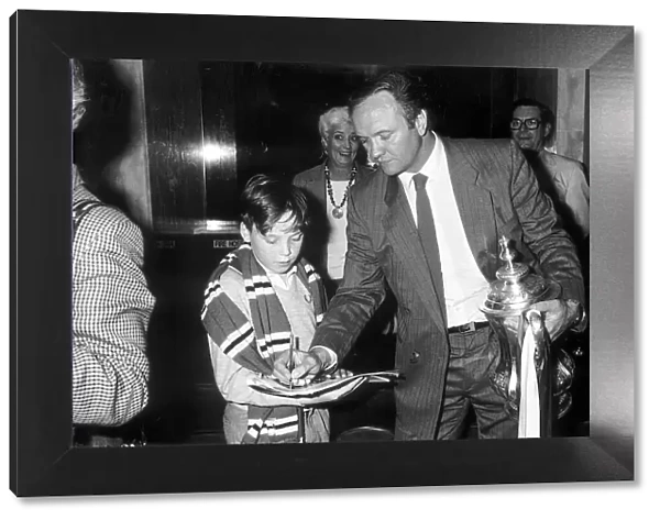 Manchester United manager Ron Atkinson signs an autograph for a young fan whilst holding