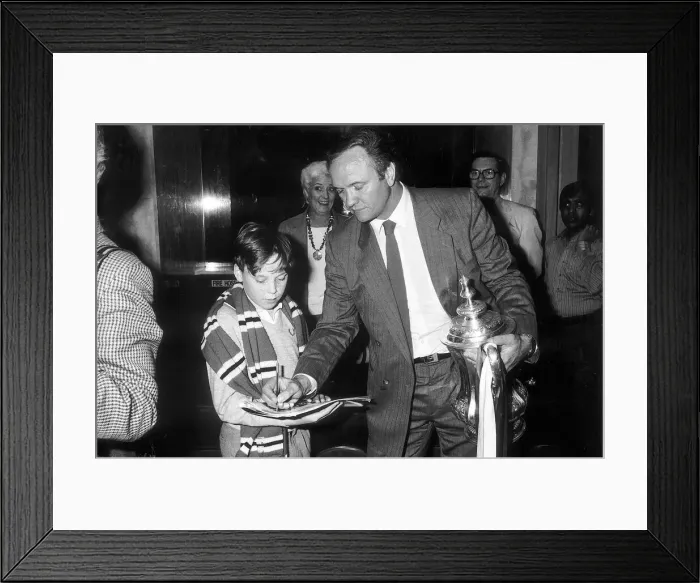 Framed Print : Manchester United manager Ron Atkinson signs an autograph for a young fan whilst holding Framed Print : Manchester United manager Ron Atkinson signs an autograph for a young fan whilst holding