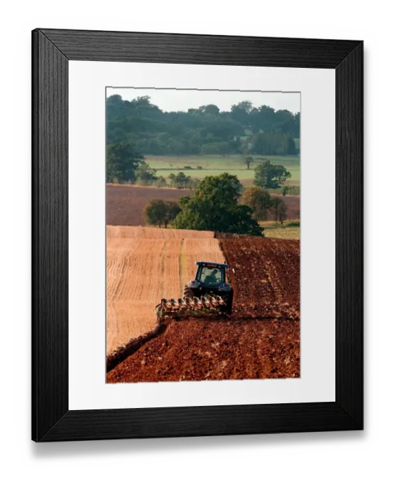Framed Print : A farm worker steers his tractor and plough in the early evening light on land Framed Print : A farm worker steers his tractor and plough in the early evening light on land