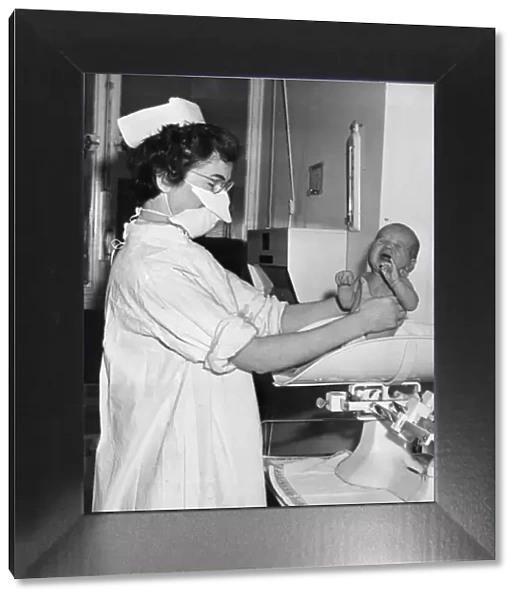 A nurse pictured holding and weighing a baby December 1956