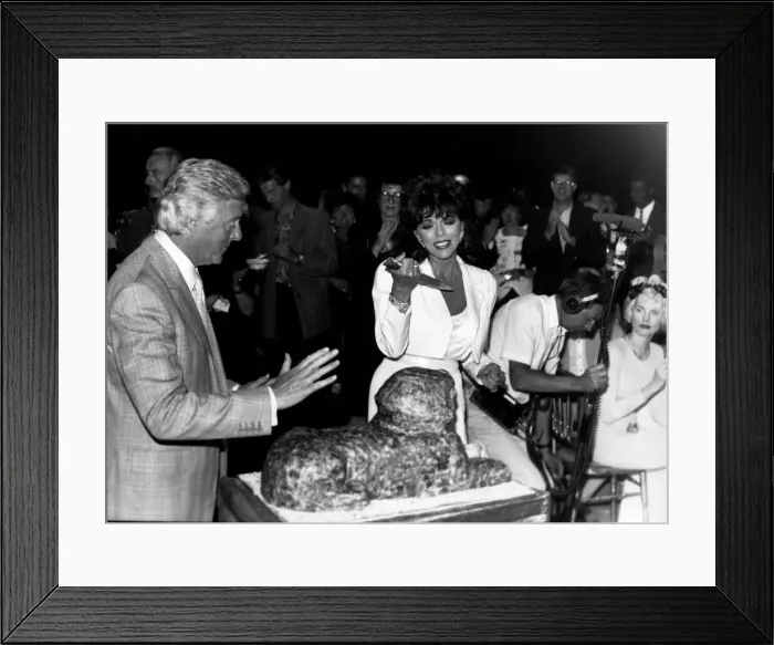 Framed Print : Joan Collins Actress frowning at cutting the cake in the shape of a Sphinx