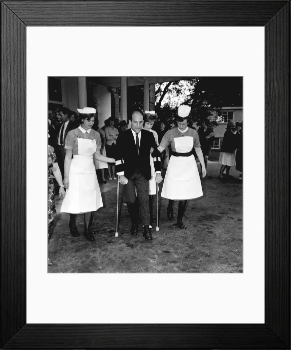 Framed Print : Stirling Moss motor racing driver leaving hospital 1962 on crutches with help of