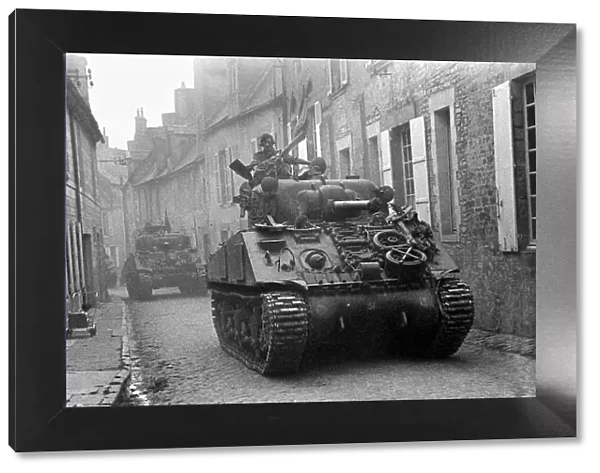 British troops in Sherman tanks roll throught the narrow cobbled streets of a Normandy