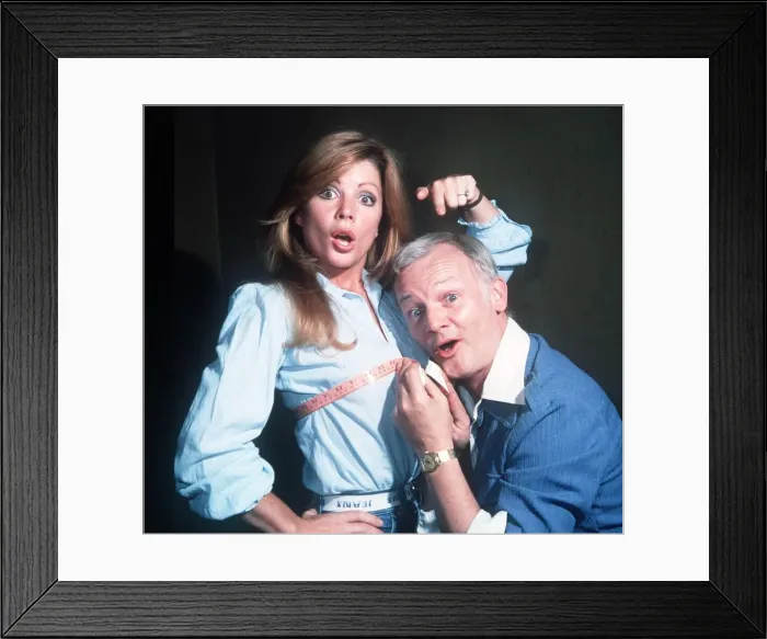 Framed Print : John Inman Comedian Actor holds a tape measure around the chest of Actress Penny Irving