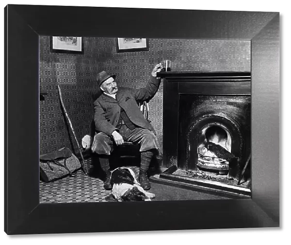 Man and his Dog - March 1935 A game keeper relaxes with his drink by the fire at