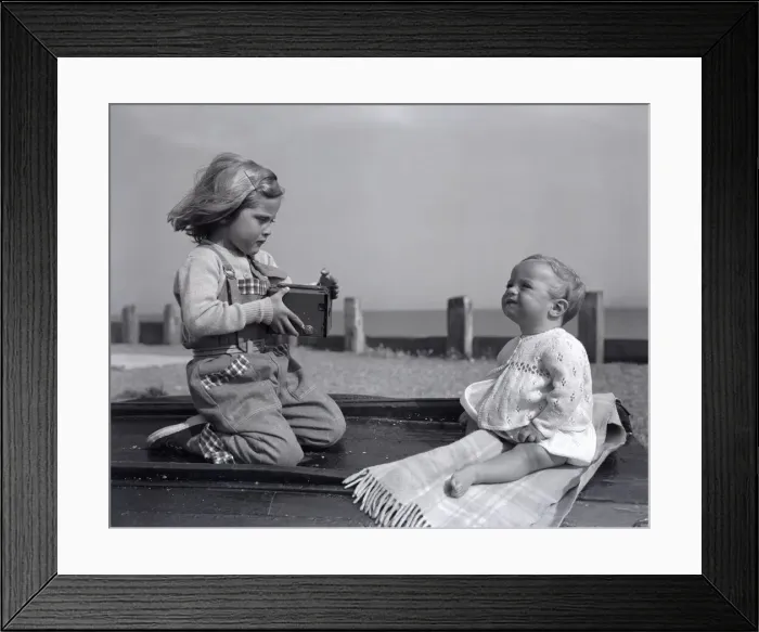 Framed Print : A small girl takes a picture of her little sister on Brighton beach whilst enjoying