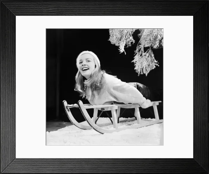 Framed Print : A model posing in the studio, lying on a toboggan. 22nd December 1957
