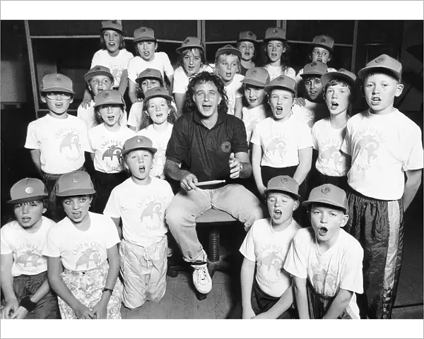 David Essex Singer surrounded by choir of school children wearing baseball caps