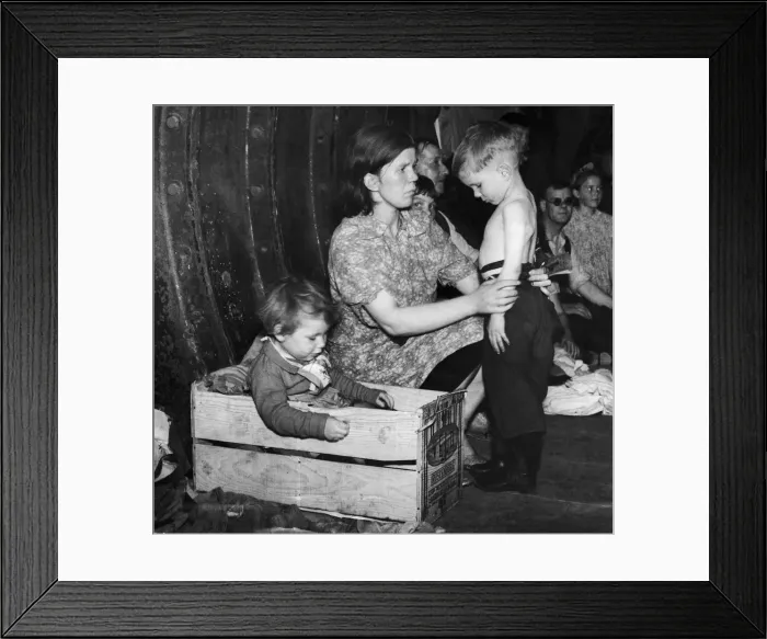 Framed Print : A mother tends to her young son while her daughter settles into a bed made from a wooden
