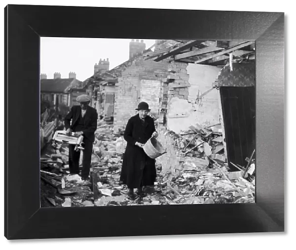 An elderly couple clear away the rubble near their homes after an air raid by the German