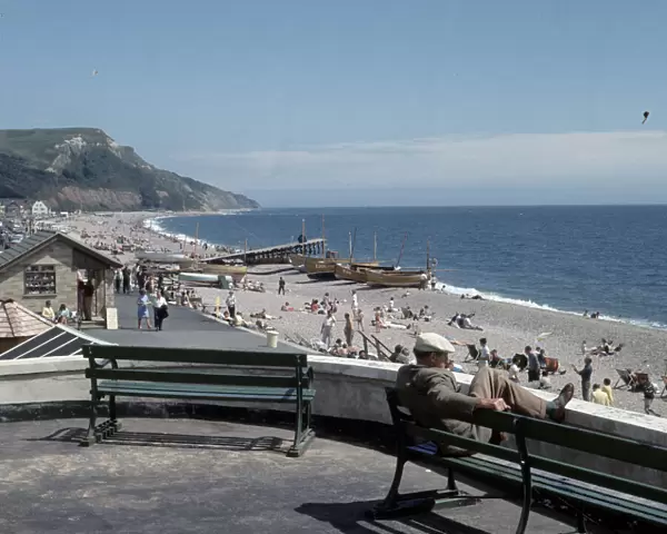 A man sitting on bench looks out over the beach at the small seaside town of Seaton