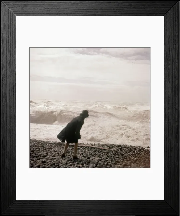 Framed Print : A woman throws one of the many beach pebbles in to the rough sea on the Sussex coast