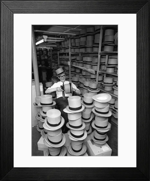 Framed Print : Man happily brushing top hats at a suit hire company in preparation for Royal Ascot