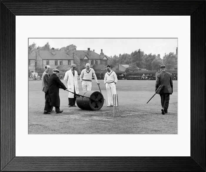 Framed Print : Longsight Cricket Club, Lancashire. Ground staff prepare the wicket while players Framed Print : Longsight Cricket Club, Lancashire. Ground staff prepare the wicket while players