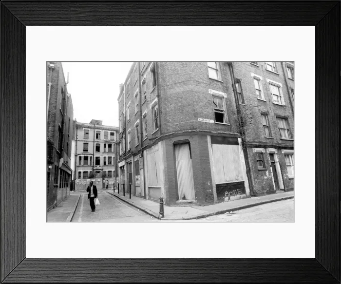 Framed Print : A man carrying his shopping bag as he walks past delapidated buildings with broken Framed Print : A man carrying his shopping bag as he walks past delapidated buildings with broken