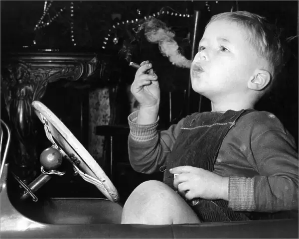 Three year old David Fellows, puffs away happily in his pedal-car, on a man-sized cigar