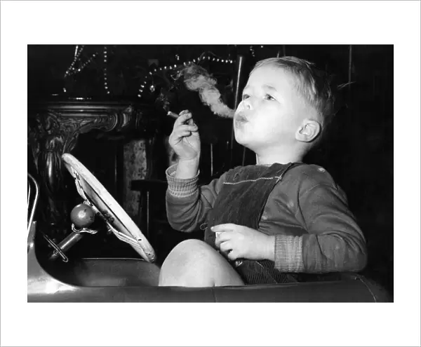 Three year old David Fellows, puffs away happily in his pedal-car, on a man-sized cigar