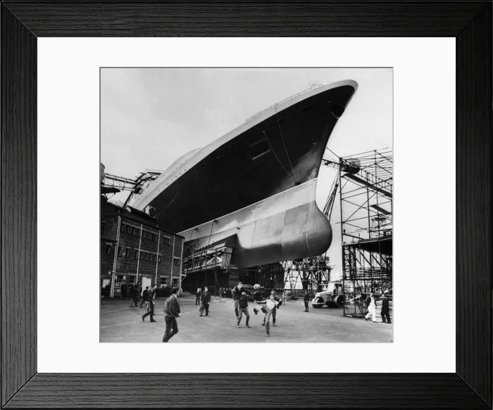 Framed Print : Ship builders playing football below the hull of the new Cunard Liner QE2 at Clyde