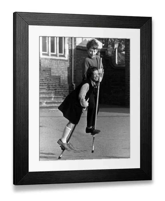 Framed Print : Boy and girl on pogo sticks in the playground. 22nd March 1967 Framed Print : Boy and girl on pogo sticks in the playground. 22nd March 1967