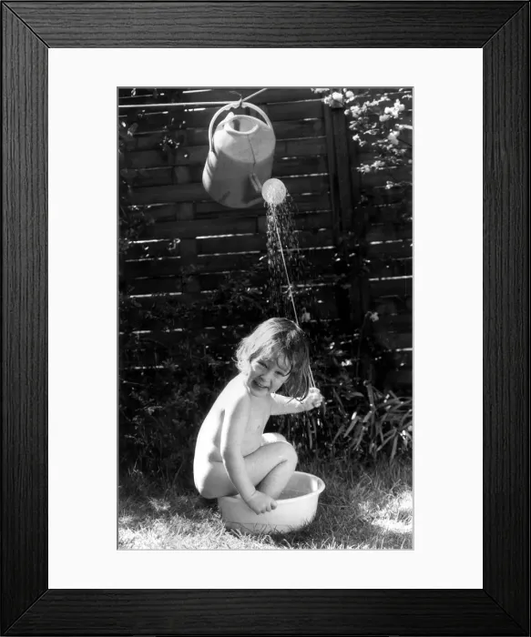 Framed Print : Three year old Tom Bardy is enjoying an improvised shower bath in the back garden of his Framed Print : Three year old Tom Bardy is enjoying an improvised shower bath in the back garden of his