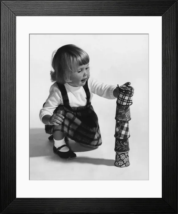Framed Print : A young girl playing with a stack of cups. March 1964
