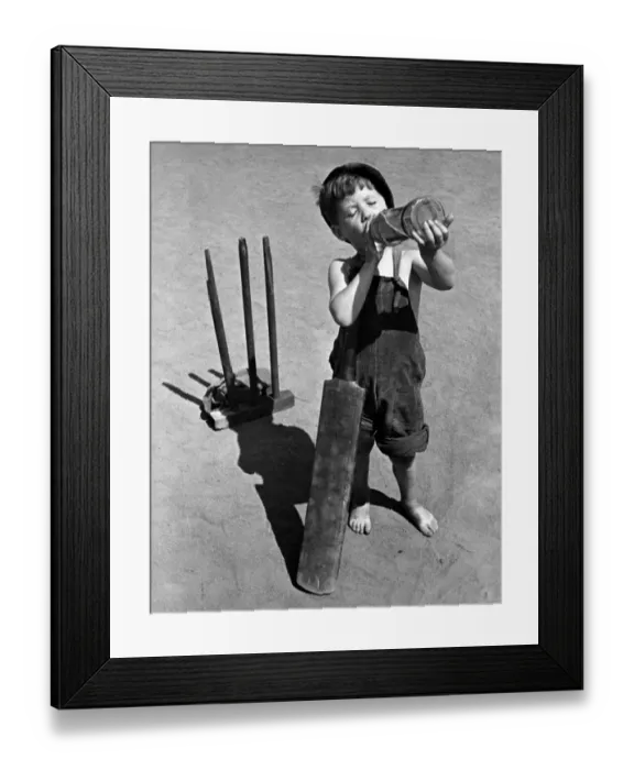Framed Print : Five year old boy enjoys a refreshing drink from a bottle whilst playing cricket on a hot
