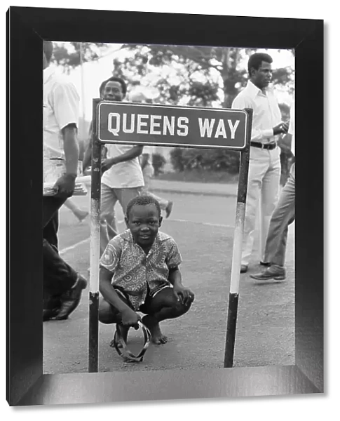 Young boy kneeling down bya road sign reading 'Queens Way'in Kampala, Uganda