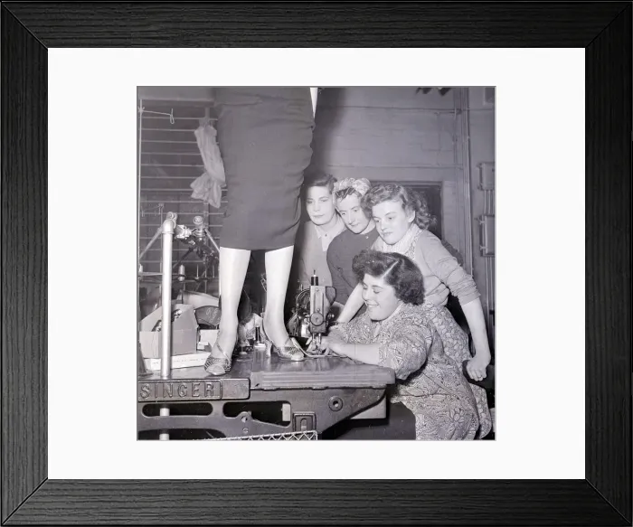 Framed Print : A lady in a pencil skirt stands on a bench while a lady sews on the sewing machine Framed Print : A lady in a pencil skirt stands on a bench while a lady sews on the sewing machine