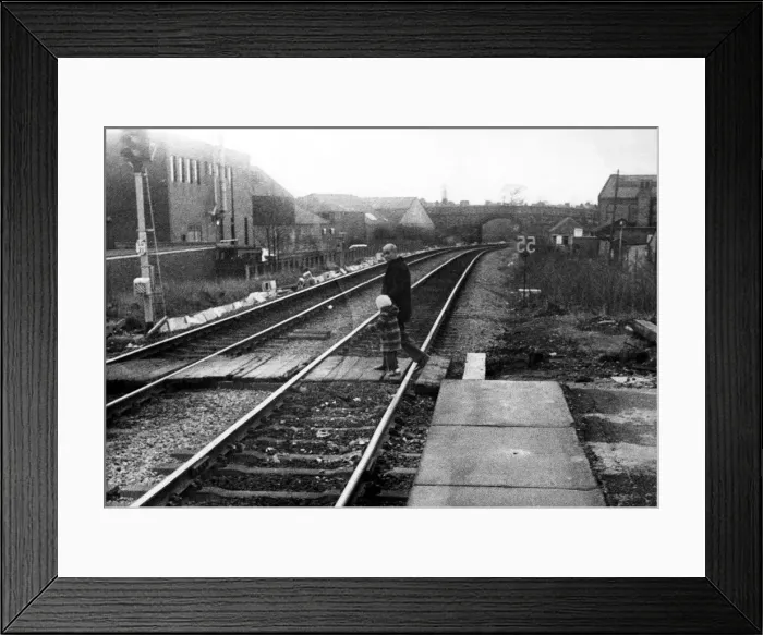 Framed Print : A man with a young child illegally crossing the railway line at West Jesmond Station