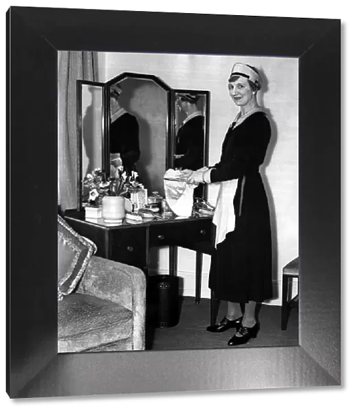 A maid standing by a dresser mirror polishing the silver, March 1938