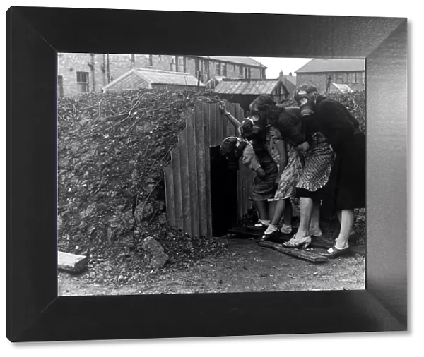 A family wearing gas masks go into an Anderson air raid shelter