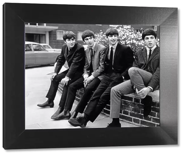 The Beatles pose sitting on a wall. Left to right: John Lennon, George Harrison
