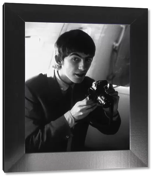George Harrison holding his camera on board the plane en route to New York, USA