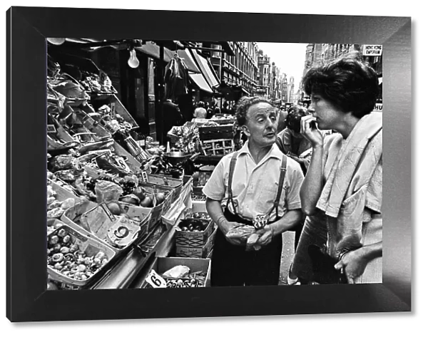 Market trader on his stall with customer in Londons Soho. 15th June 1964
