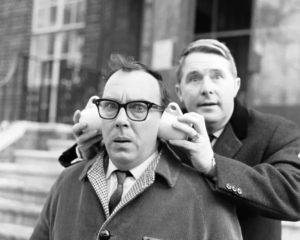 Eric Morecambe gets a new style in ear muffs with coffee cups from his partner