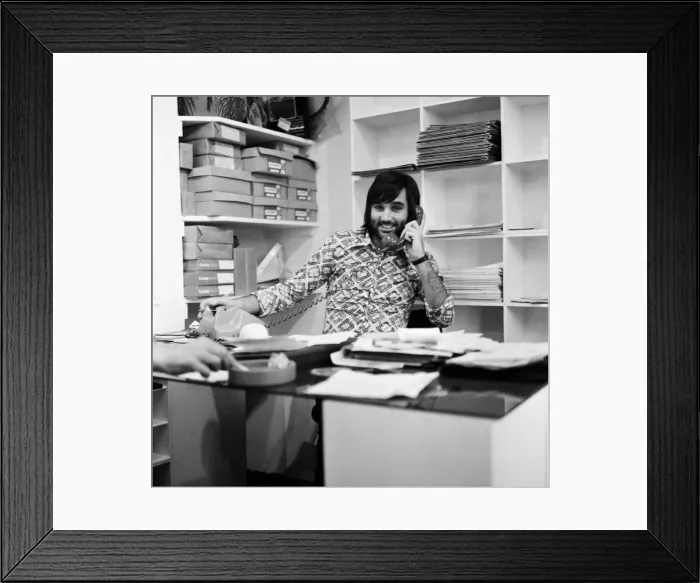 Framed Print : Footballer George Best, business man on the phone sitting at desk in his shop