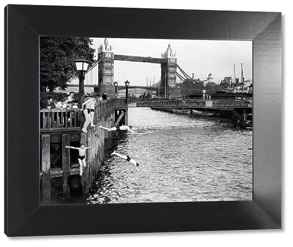 Boys jumping off the bank of the River Thames into the water near Tower Bridge, London