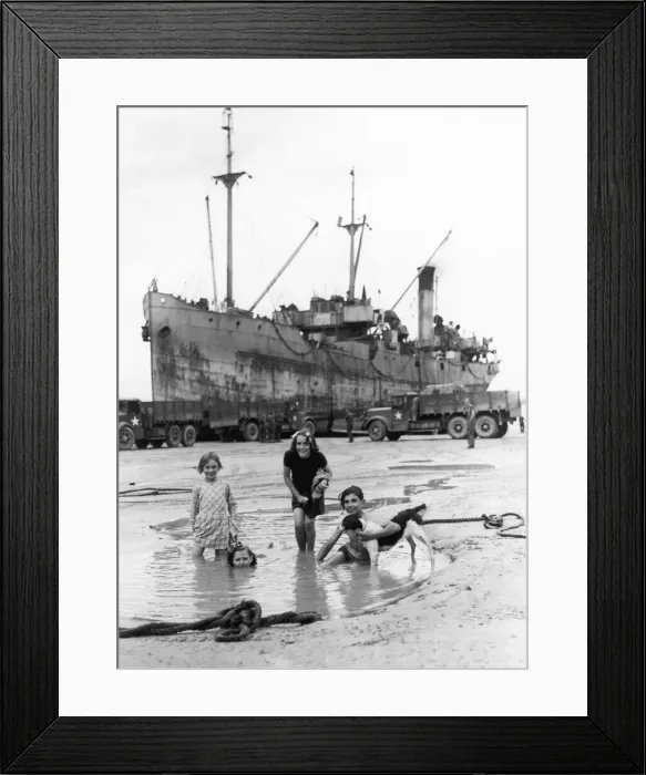 Framed Print : French children playing in a pool on the beach at Arromanches while a ship discharges its Framed Print : French children playing in a pool on the beach at Arromanches while a ship discharges its
