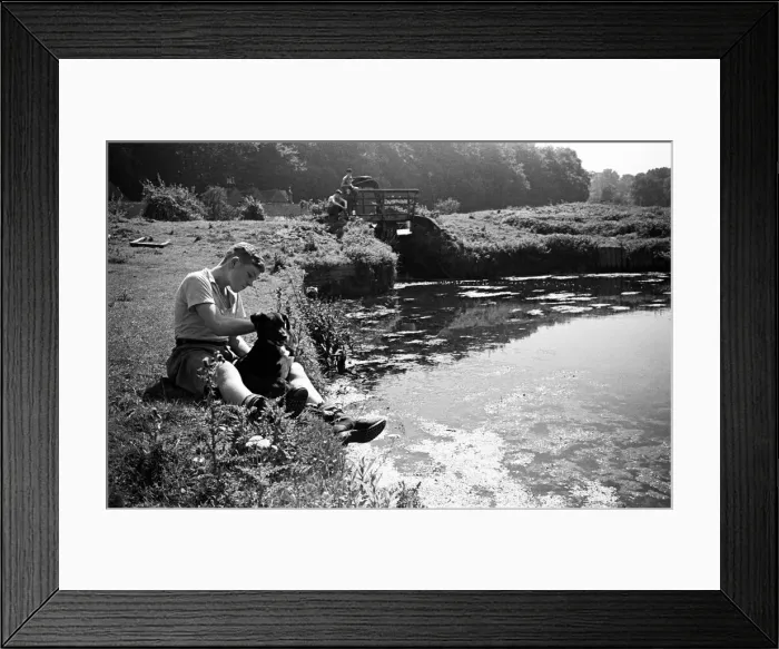 Framed Print : A boy sits with his pet dog next to the River Chess in Chenies, Buckinghamshire