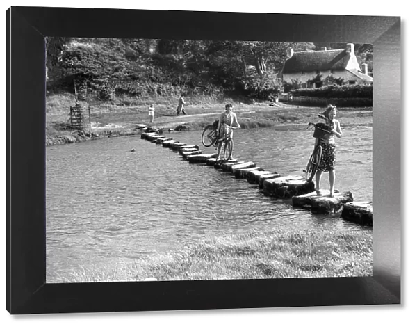 A couple of young women use stepping stones to cross the Ewenny River that rises to