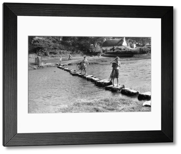 Framed Print : A couple of young women use stepping stones to cross the Ewenny River that rises to Framed Print : A couple of young women use stepping stones to cross the Ewenny River that rises to