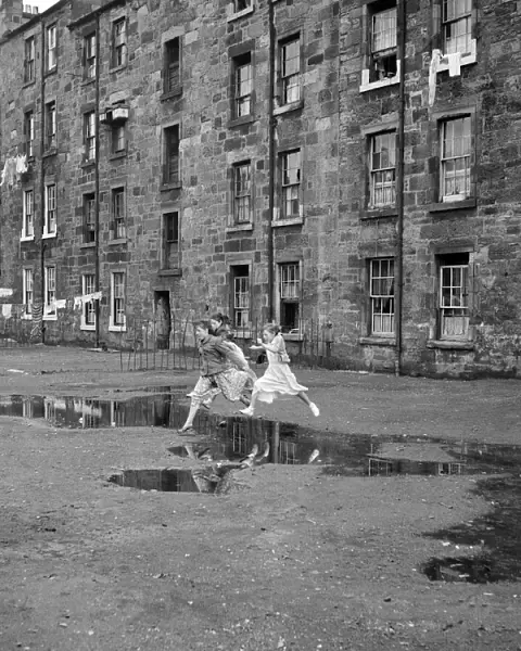 Three young friends leap over a puddle outside a Govan tenement block in Glasgow