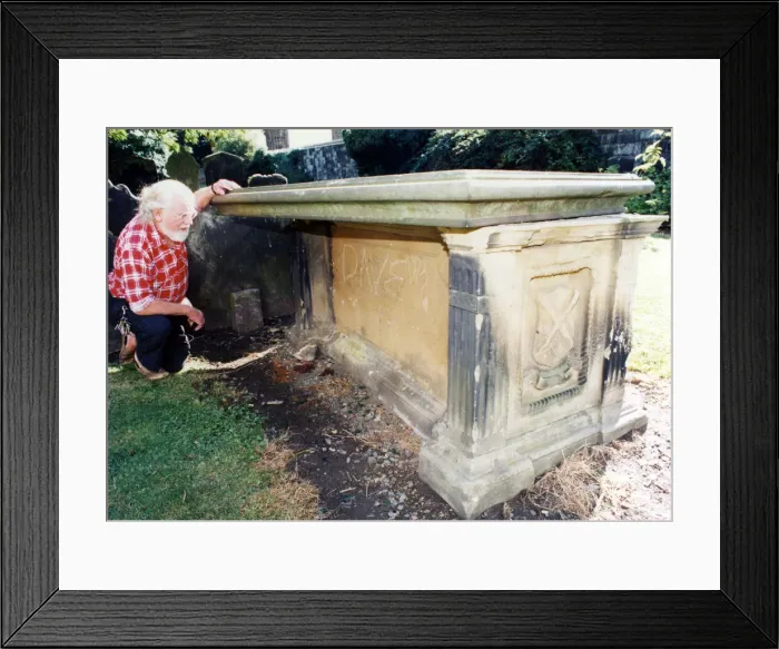Framed Print : St Nicholas church tomb, church warden Ken Brookfield examines a tombstone in