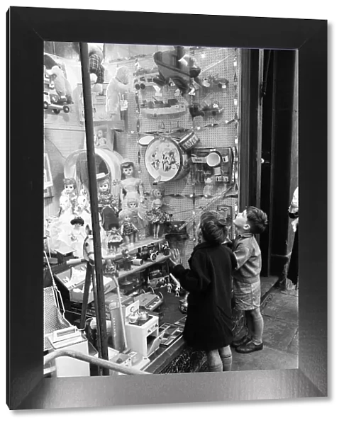 Children look longingly at toys into shop window at Christmas, 16th December 1960