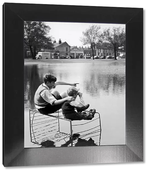 Two boys sitting on an old fire guard on the edge of a lake. 1st July 1955